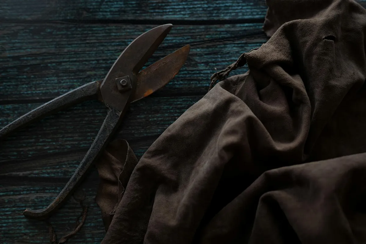 Brown fabric and a pair of scissors on a dark wooden surface