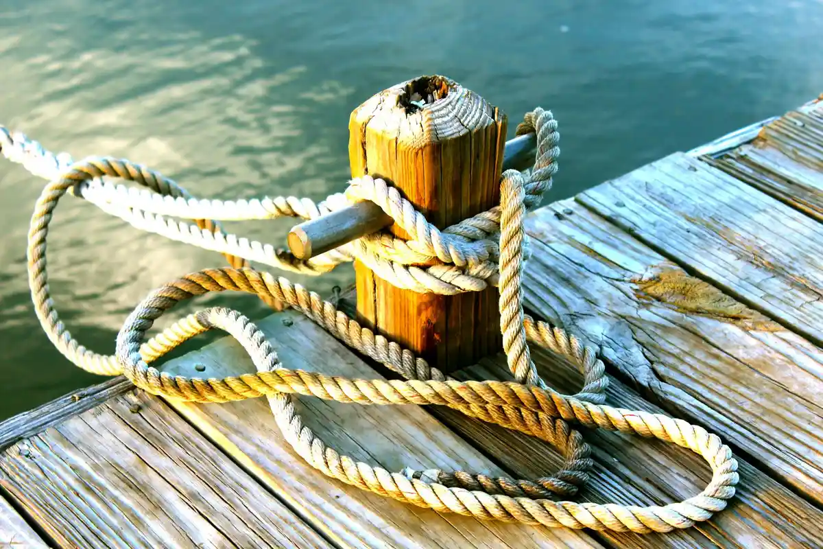 Nylon rope coiled and tied around a weathered wooden post on a dock beside calm water.