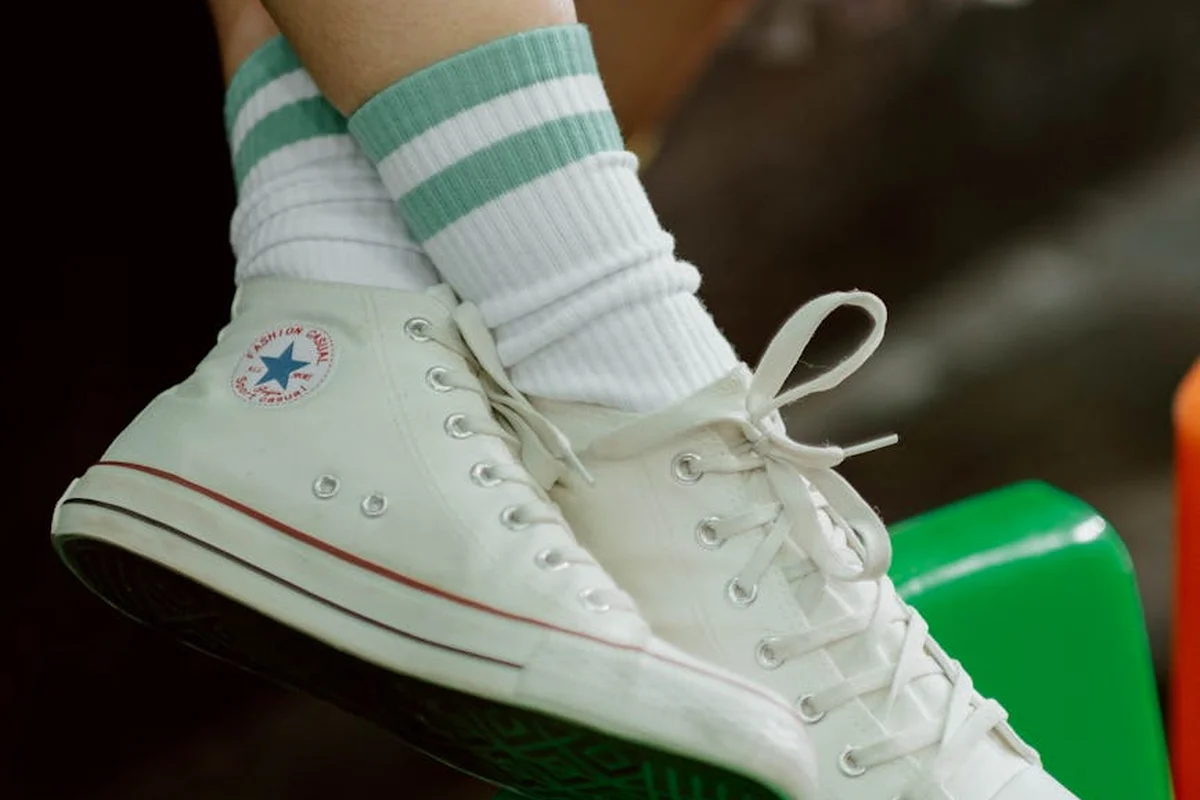 White canvas sneaker with a blue star logo and mint-green striped socks resting on a green surface.