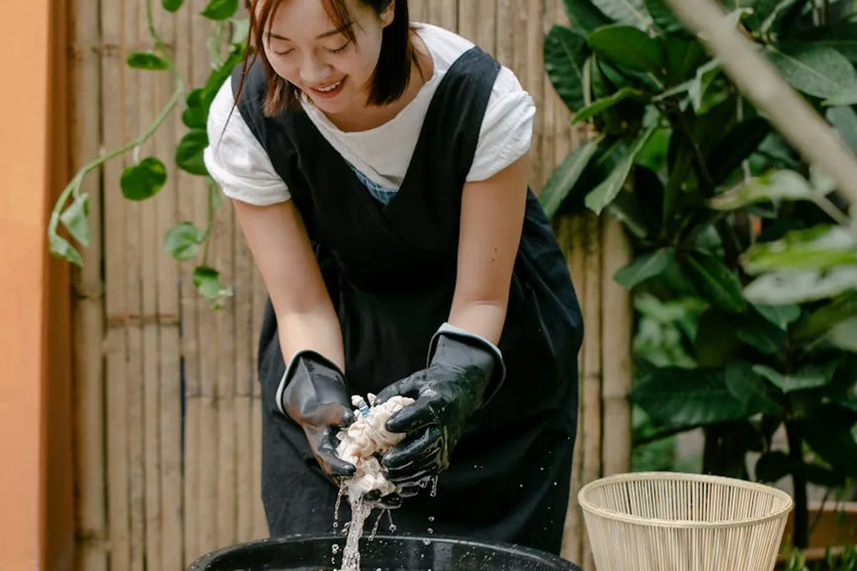 Person wearing gloves wringing fabric over a bucket outdoors