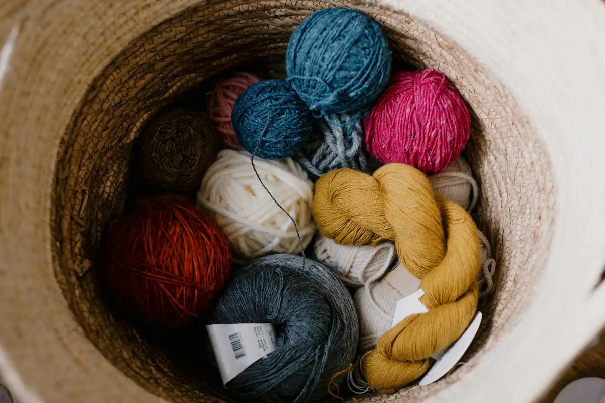 Top-down view of a woven basket filled with colorful yarn skeins in red, blue, teal, white, gray, and yellow.