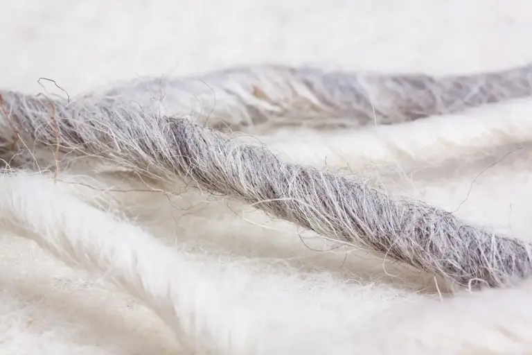 Close-up of delicate, fluffy cashmere fibers with a pale gray twisted strand resting on a light background.