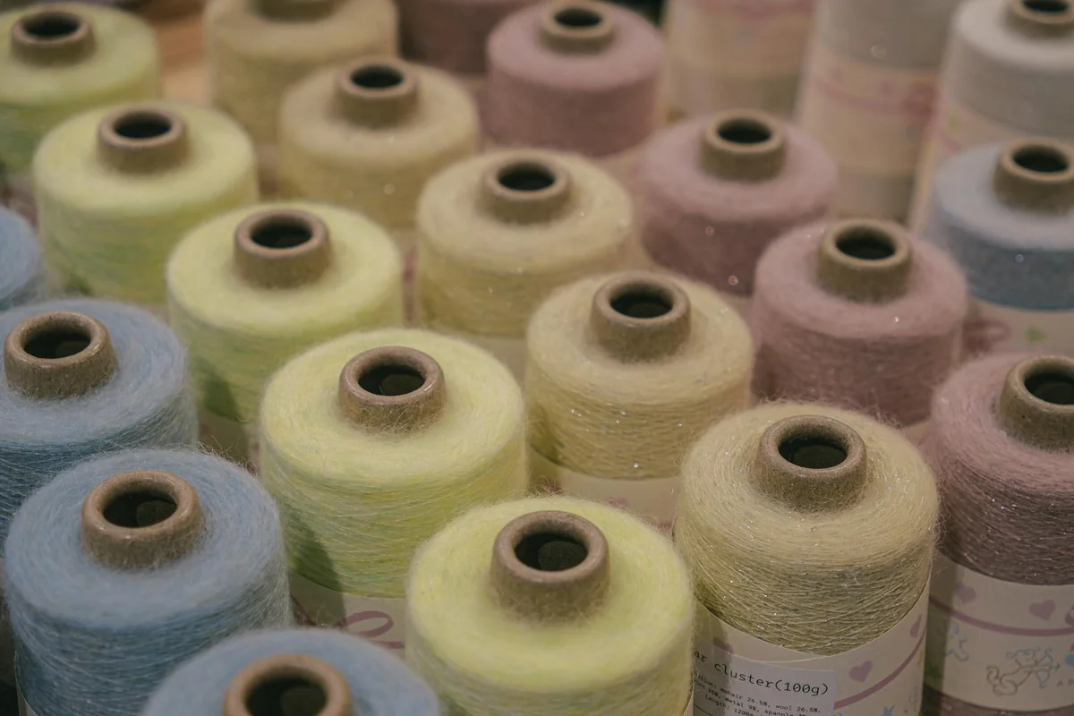 Rows of pastel-colored acrylic yarn spools arranged in a grid, featuring blues, greens, yellows, and pinks.