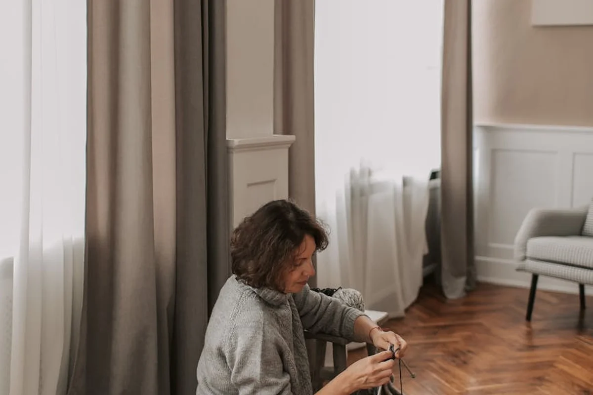 Person seated on the floor sewing knit fabric indoors, in a cozy room.