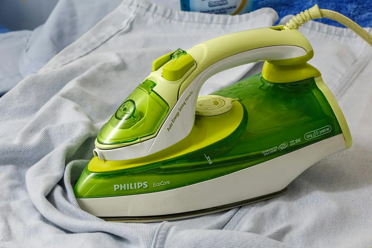 Green Philips steam iron resting on light gray fabric, ready for steaming.