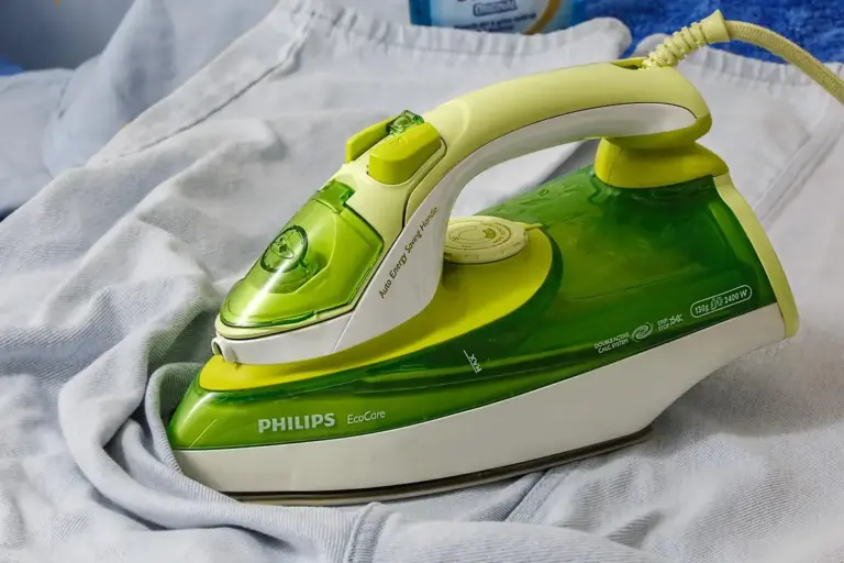 Green and white Philips steam iron resting on soft fabric, illustrating equipment used in fabric stiffening techniques.