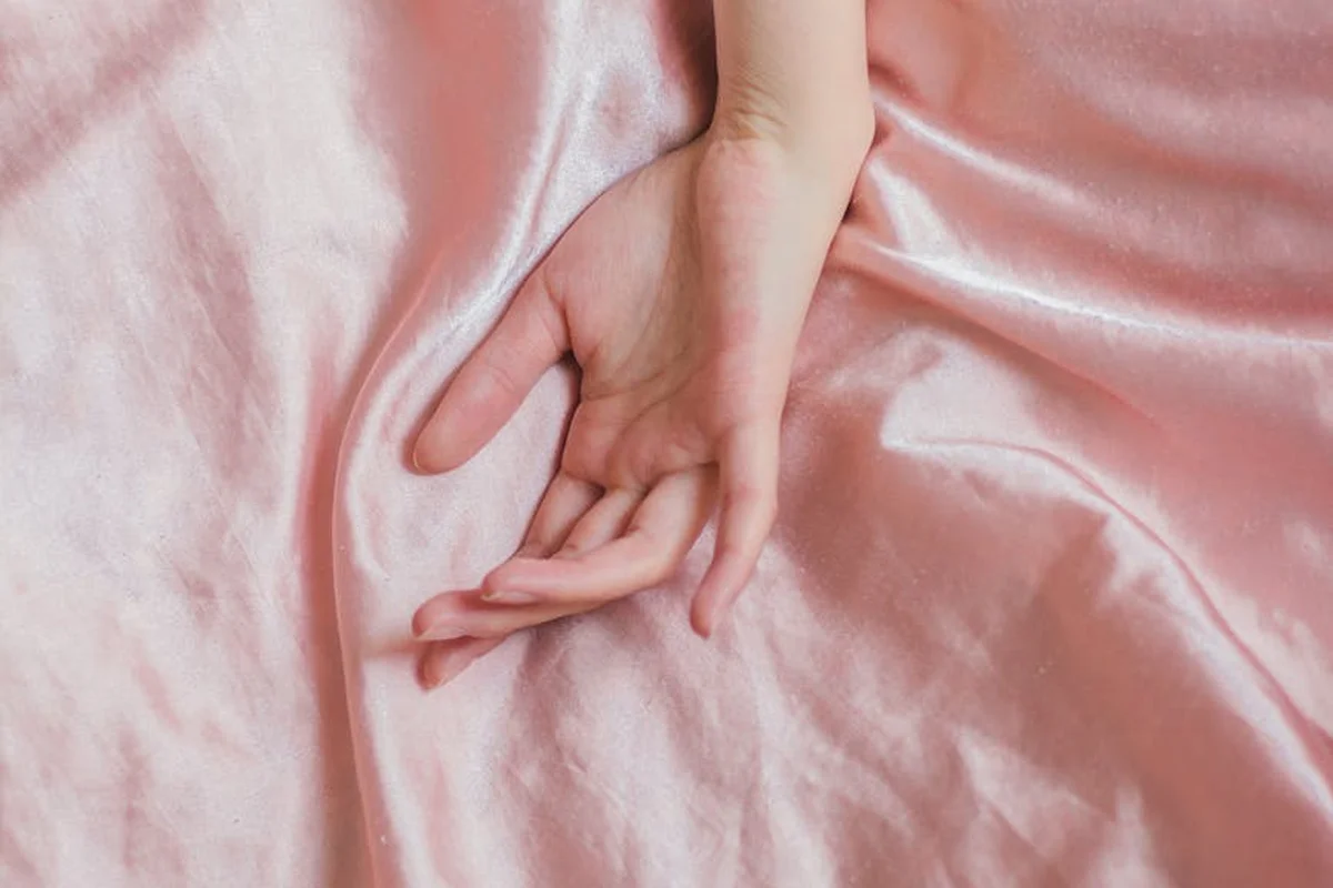 Close-up of a hand resting on soft pink satin fabric