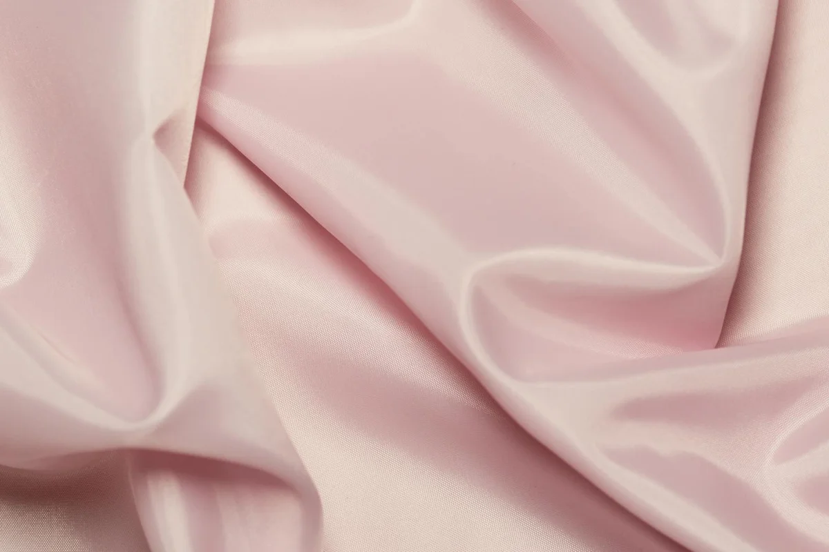 Close-up of soft pink satin-like fabric with gentle folds, illustrating texture in viscose and rayon blends