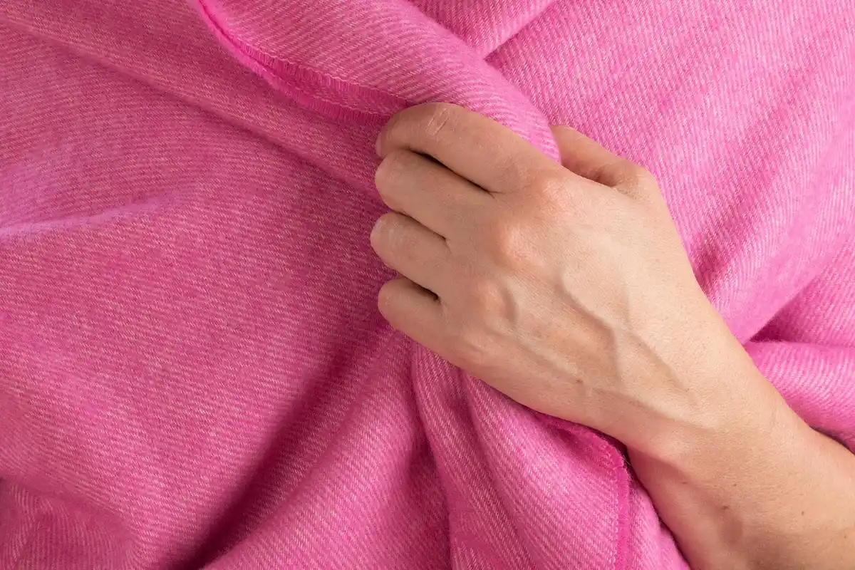 Close-up of a hand gripping pink cashmere knit fabric, showing its soft, fuzzy texture.