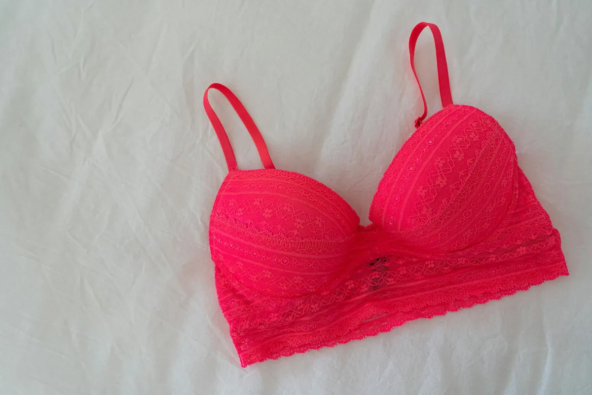 Bright pink lace bra laid flat on a light background, showing delicate undergarment fabric