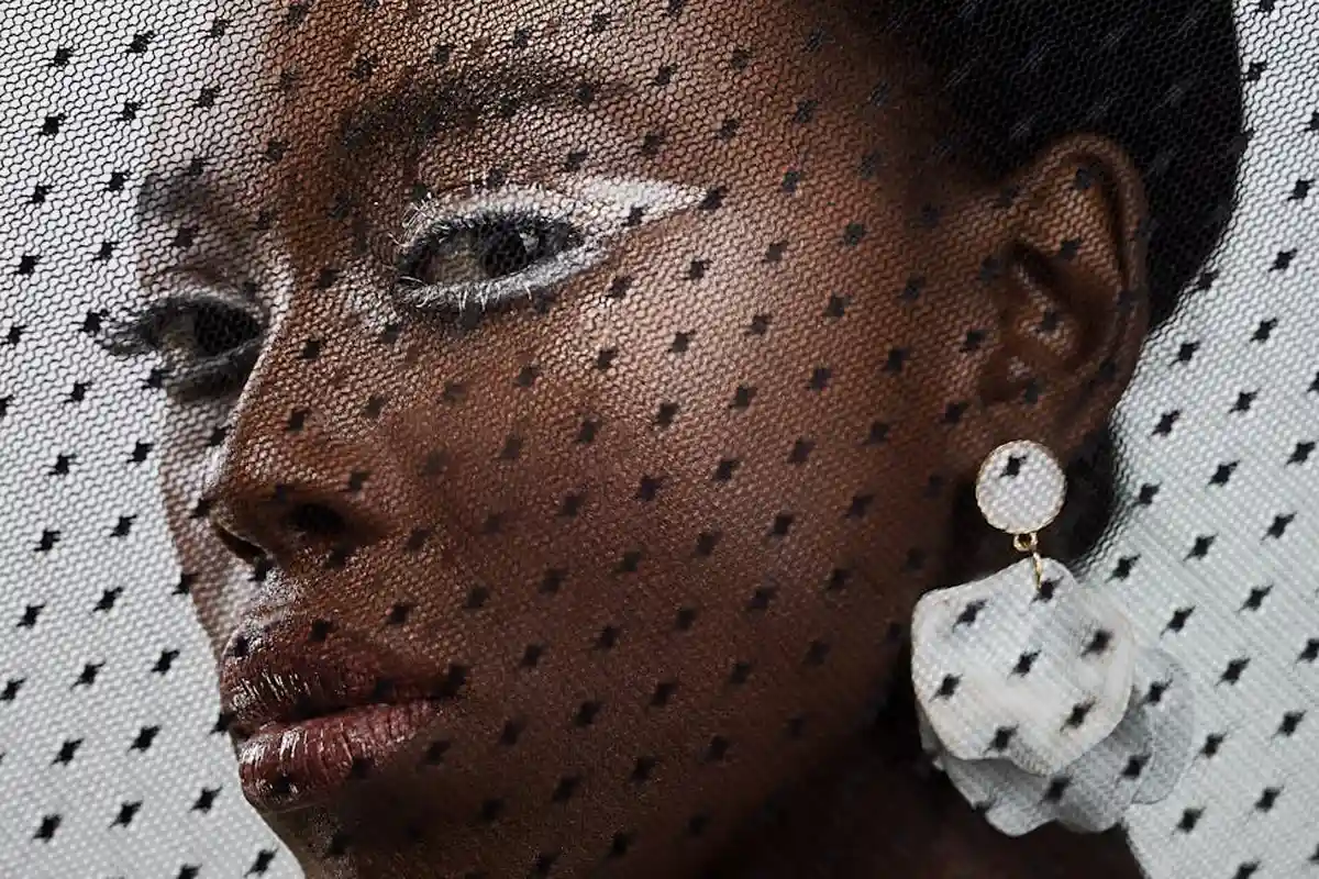 Close-up of a woman's face behind a sheer polka-dot mesh fabric, highlighting texture and patterns common to synthetic fabrics.