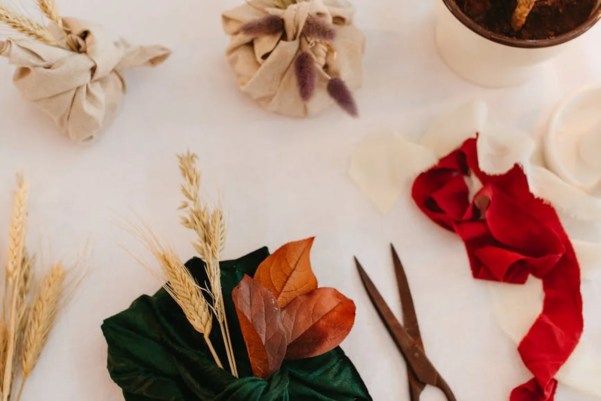 Flat lay of fabric swatches, scissors, and dried botanical stems on a light, neutral background.