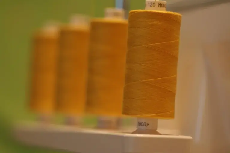 Close-up of orange polyester thread spools on a display with a blurred workshop background