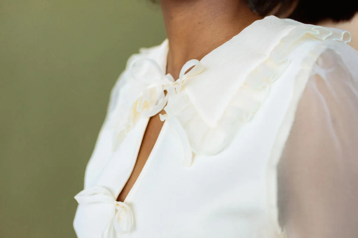 Close-up of a white blouse with decorative bows and sheer sleeves, highlighting the smooth polyester fabric.