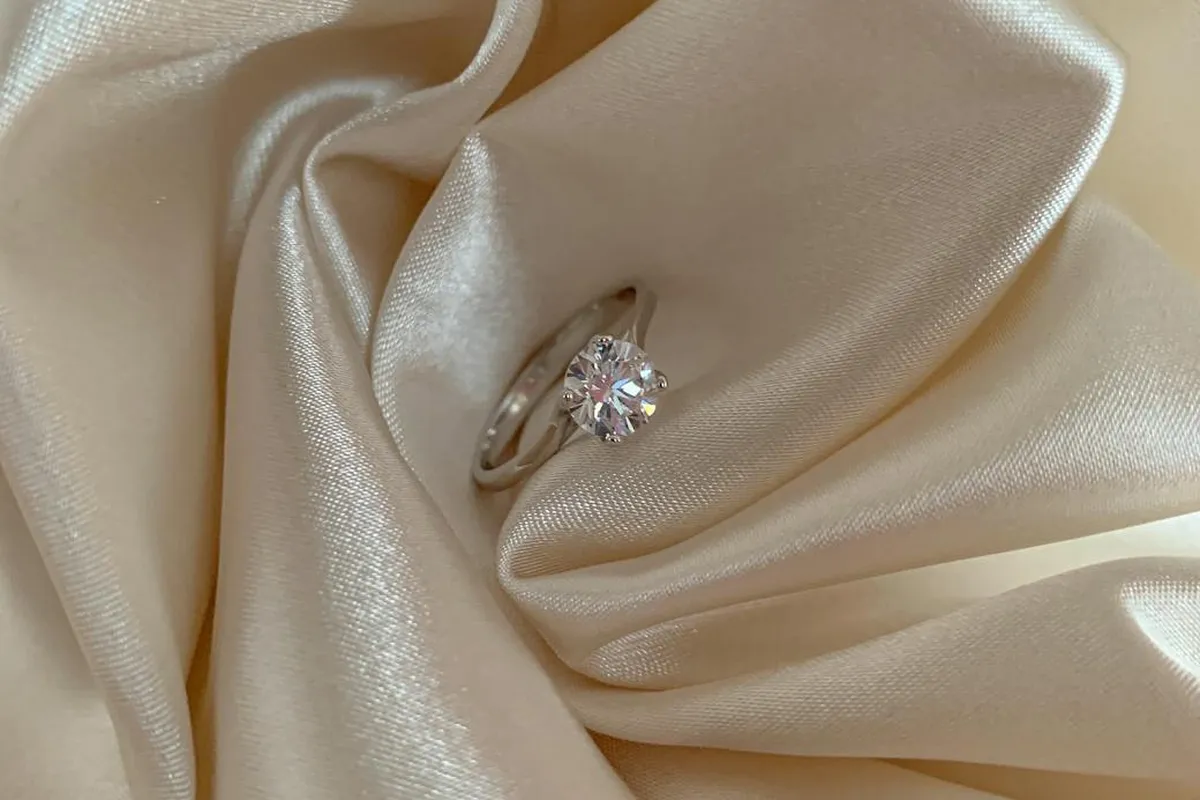 Close-up of a diamond ring resting on cream satin fabric, highlighting the smooth sheen and soft folds of polyester satin.