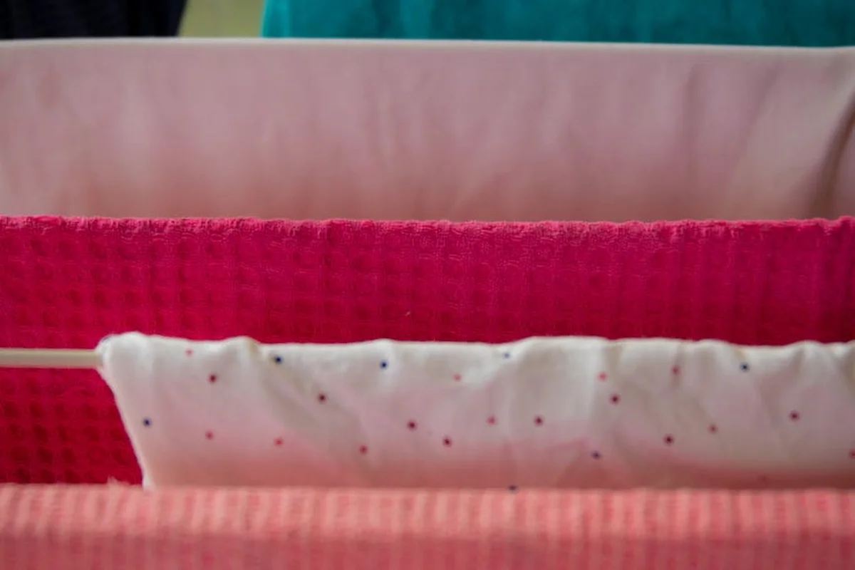 Close-up of colorful folded fabrics hanging on a clothesline, including pink, red, and white with small polka dots, drying after washing.
