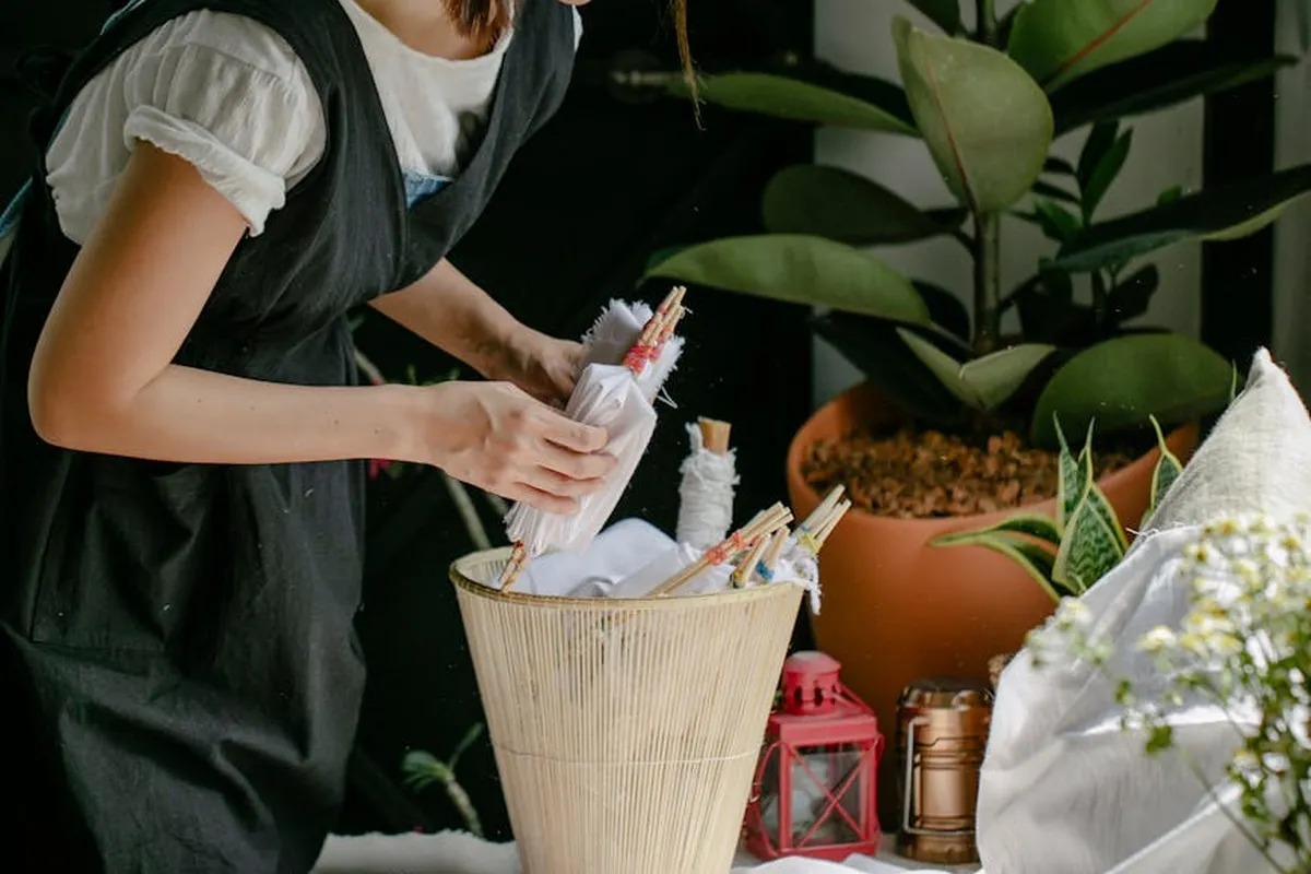 Person in a black apron arranges dye brushes and bottles on a table with plants in the background.
