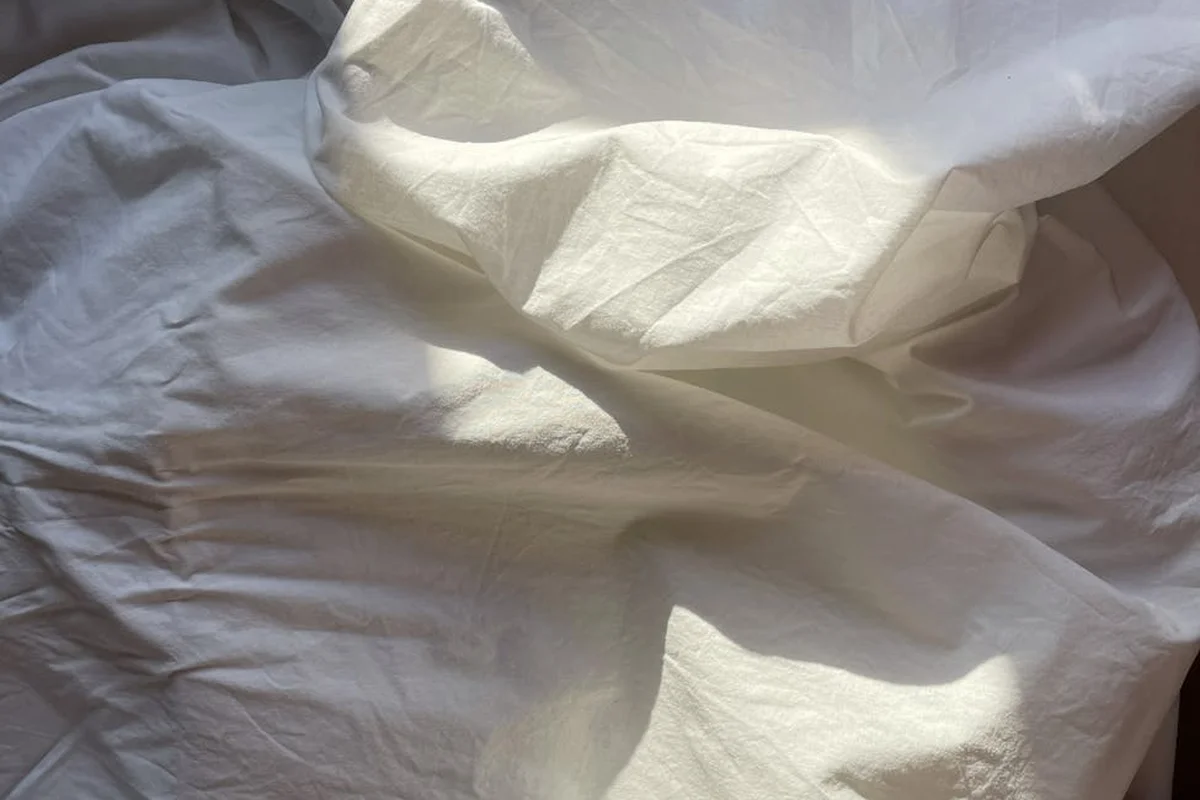 White linen fabric with soft folds and gentle shadows, illustrating care and prep for washing and storage.