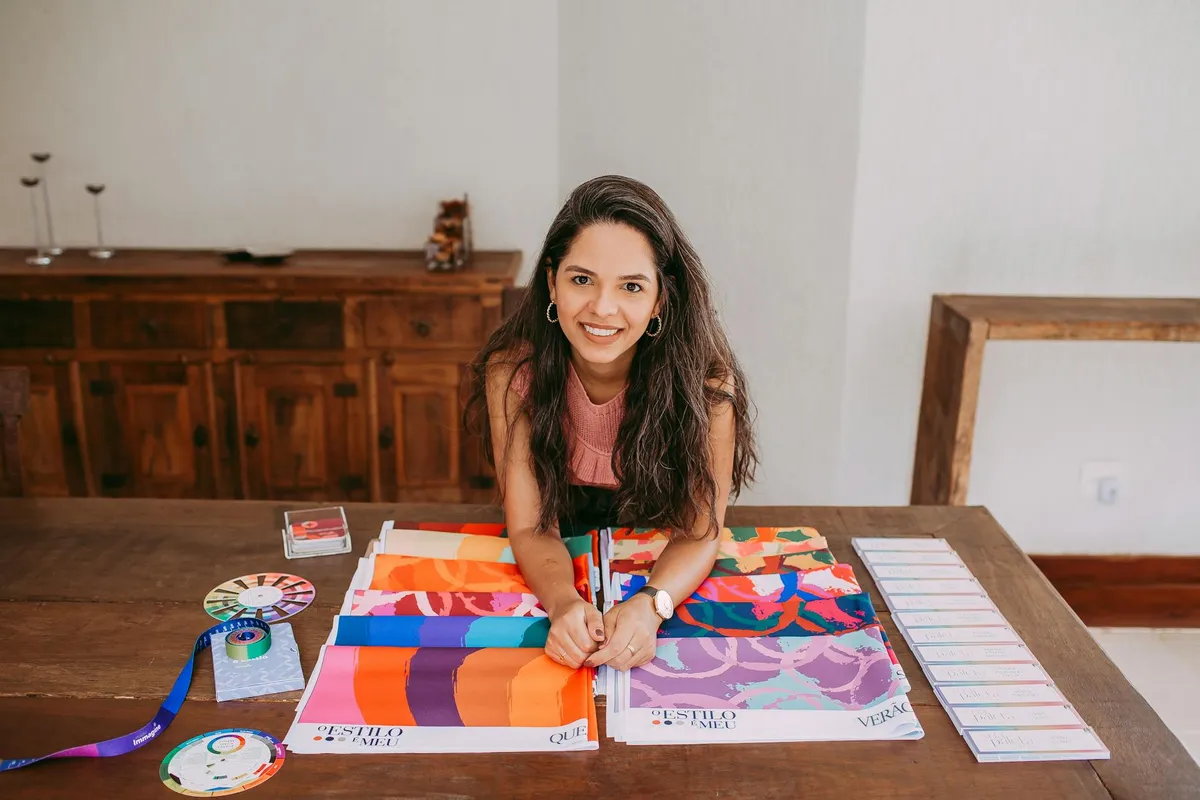 A woman sits at a wooden table, examining fabric swatches and color charts for wardrobe planning.