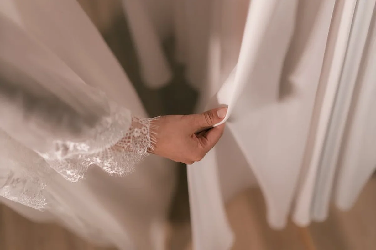 Hand grasping a sheer, white lace-sleeved garment, highlighting delicate handling of pure rayon fabric.