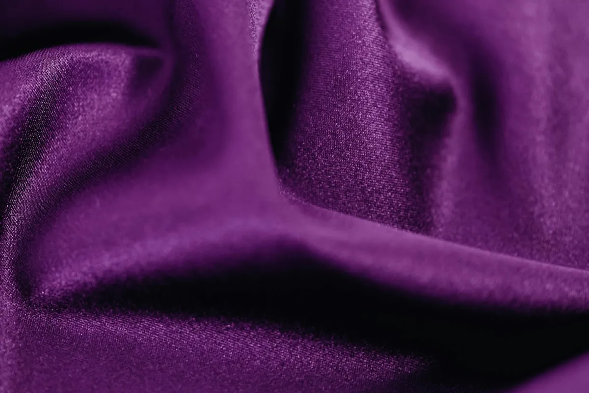 Close-up of a rich purple satin-like fabric with smooth folds and a lustrous sheen.