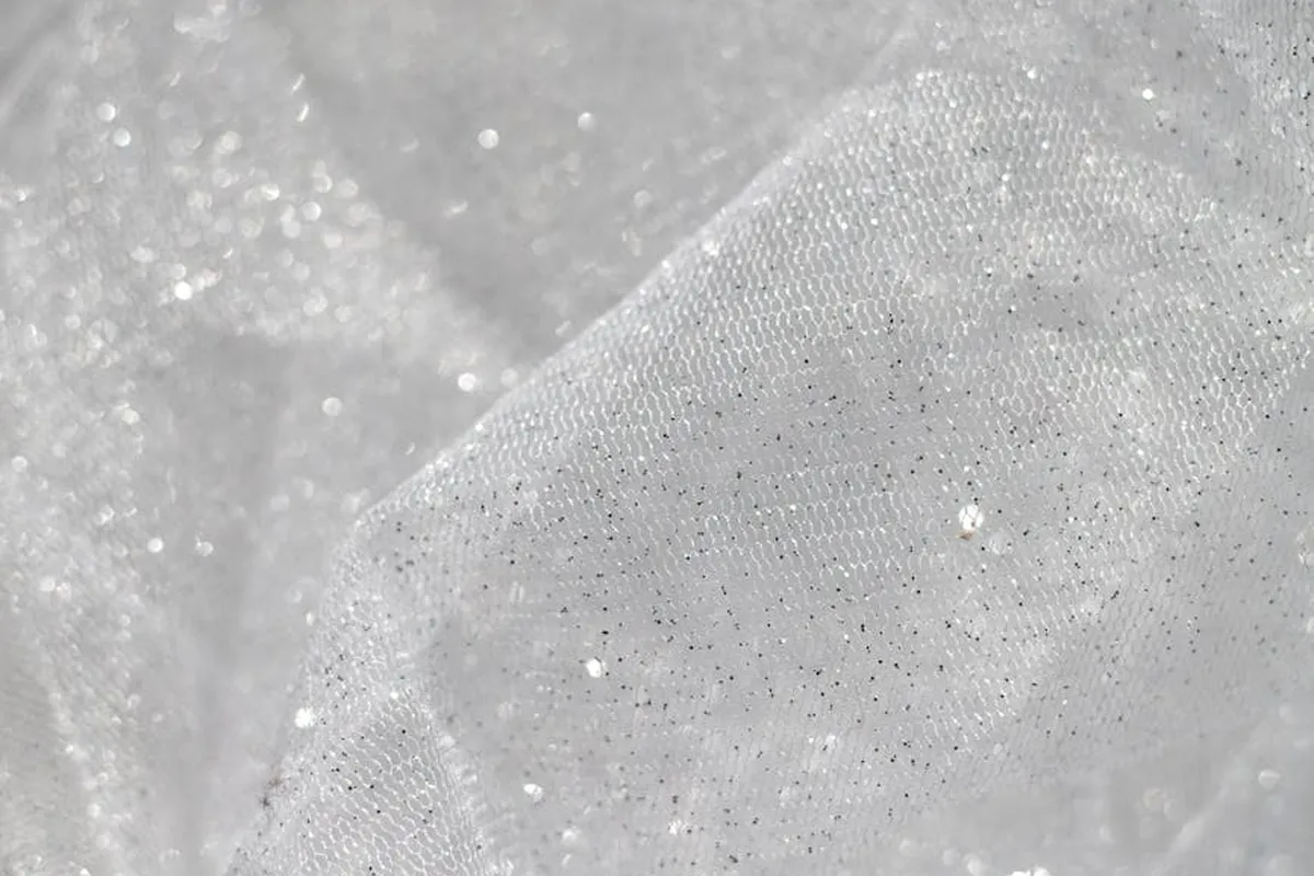 Close-up of a sheer, sparkly fabric with a fine weave and shimmering specks.