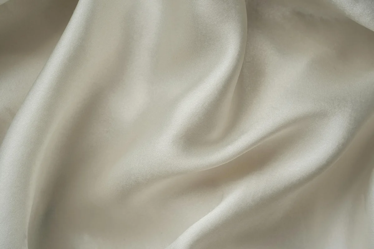 Close-up of cream-colored satin fabric with soft, flowing folds