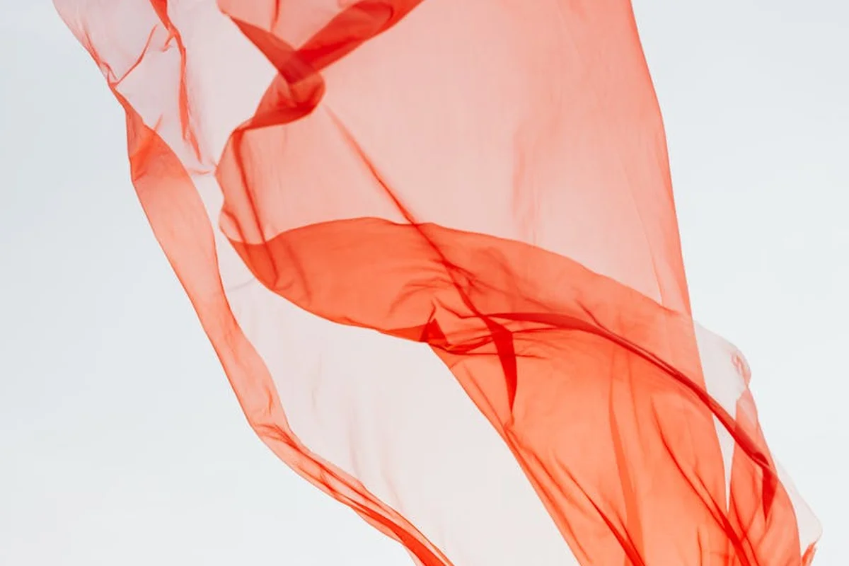 Flowing red-orange fabric fluttering against a pale background