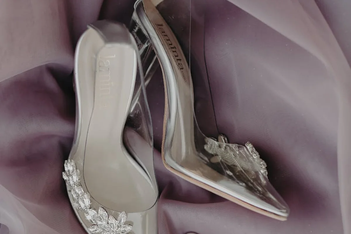 Pair of clear-strap high-heeled sandals with rhinestone embellishments resting on purple satin fabric.