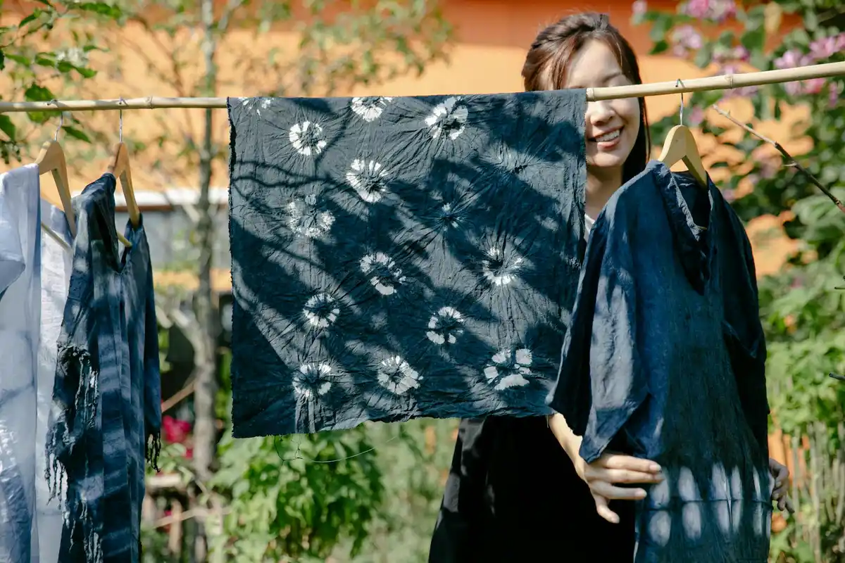 Outdoor scene with dyed fabrics hung on a clothesline; a person stands in the background.
