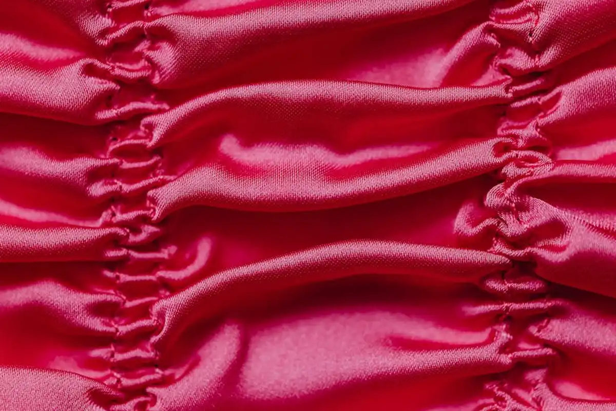 Close-up view of a bright pink ruched silk fabric with a glossy satin finish and gathered folds.