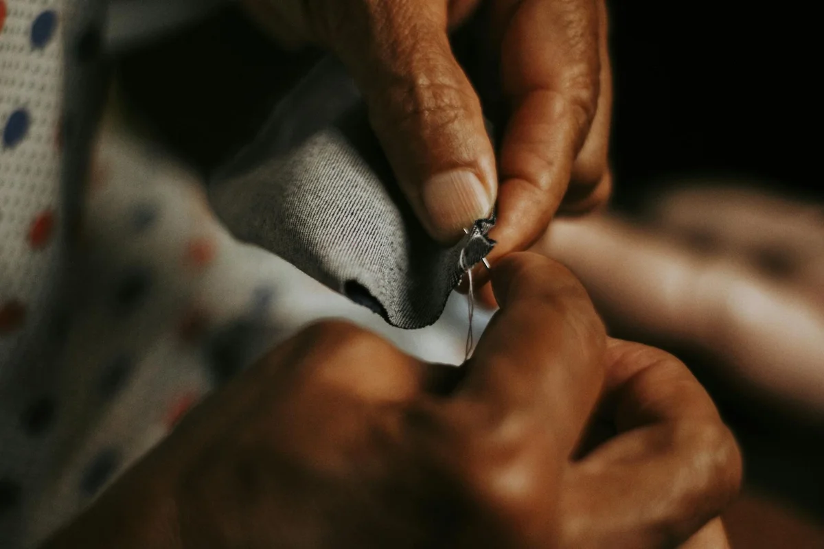 Close-up of hands sewing a tear in linen fabric using a needle and thread