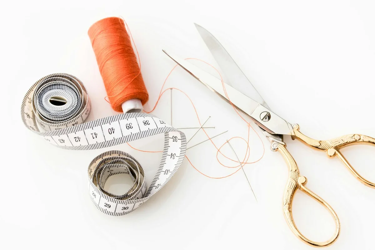 Scissors, a measuring tape, and orange thread on a white surface