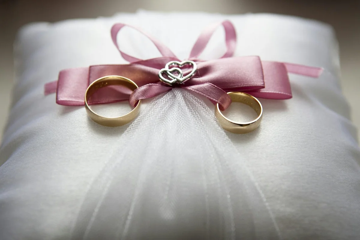 Two gold wedding bands tied with a pink ribbon resting on white silk fabric