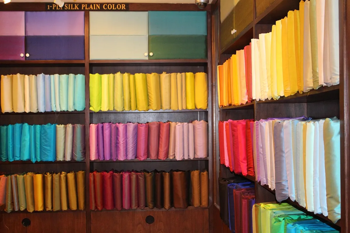 Rows of colorful silk fabric swatches arranged on shelves, displaying a broad spectrum of hues from blues and greens to reds, yellows, and purples.