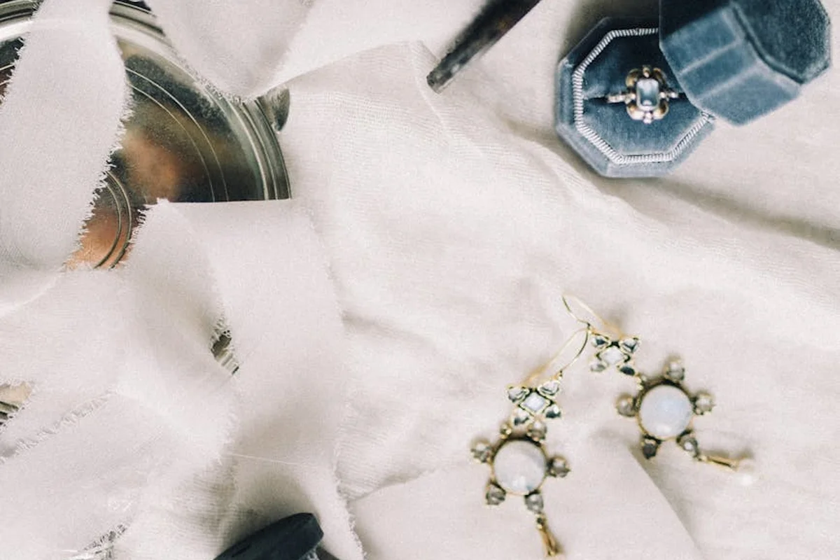 A flat lay of delicate white silk fabric with sewing tools and jewelry on a soft surface, illustrating care and handling of silk.
