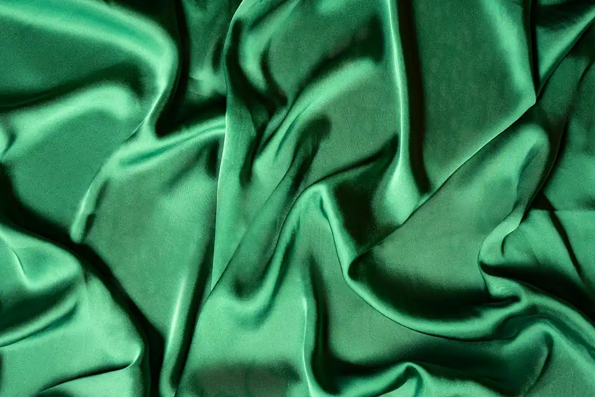 Close-up of emerald-green silk fabric with flowing folds and a lustrous sheen
