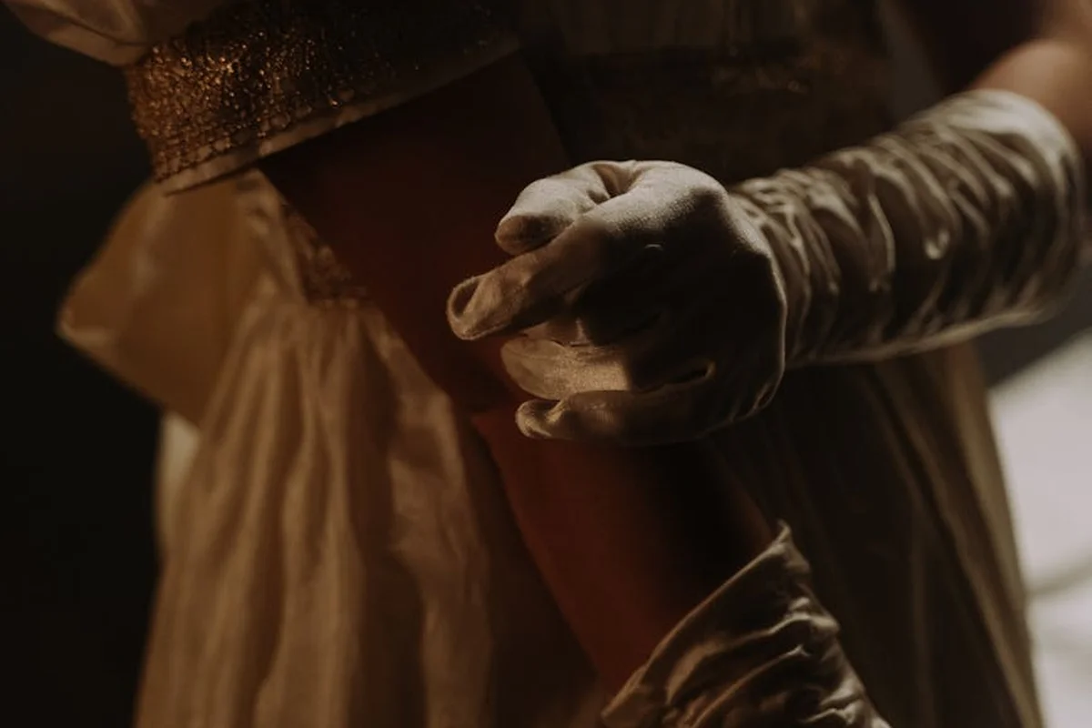 Close-up of gloved hands handling fabric in a dim workshop, illustrating careful conservation work on silk.