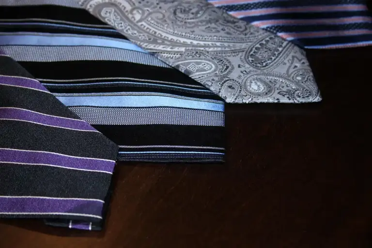 Several silk neckties with striped and paisley patterns laid on a dark wooden surface