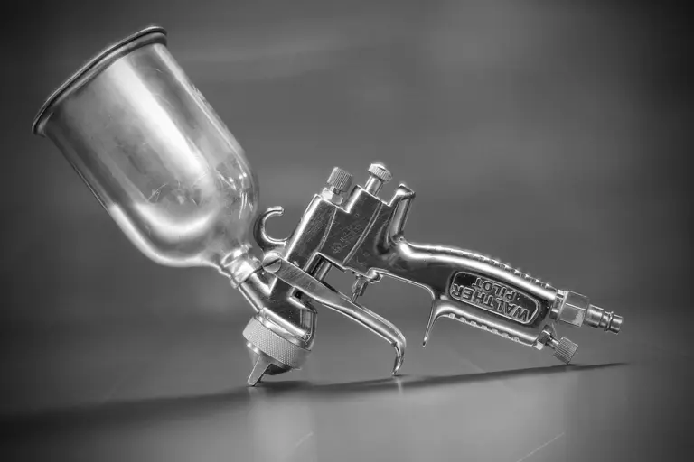 Close-up of a metal spray gun resting on a surface, used for applying liquid coatings.