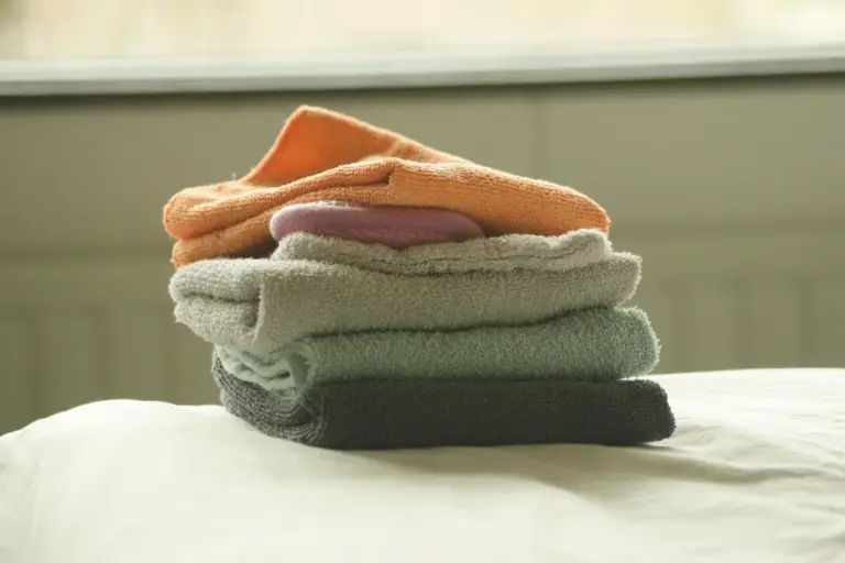 A stack of folded towels in orange, purple, white, mint green, and dark gray on a bed