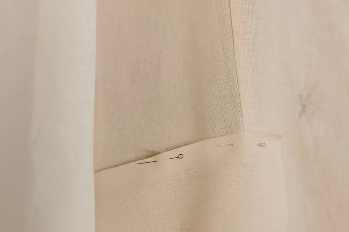 Close-up of beige fabric edge with pins, prepared for starching