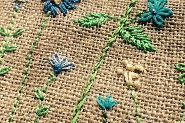 Close-up of colorful embroidered flowers on coarse burlap fabric, highlighting texture and vibrant colors.