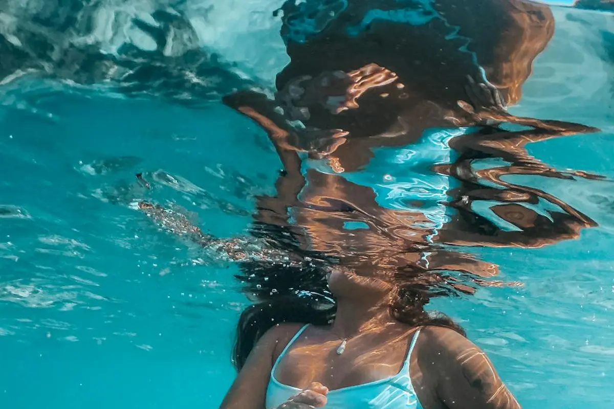 Underwater scene of a person wearing a light blue bikini top, submerged in turquoise water with light reflections.