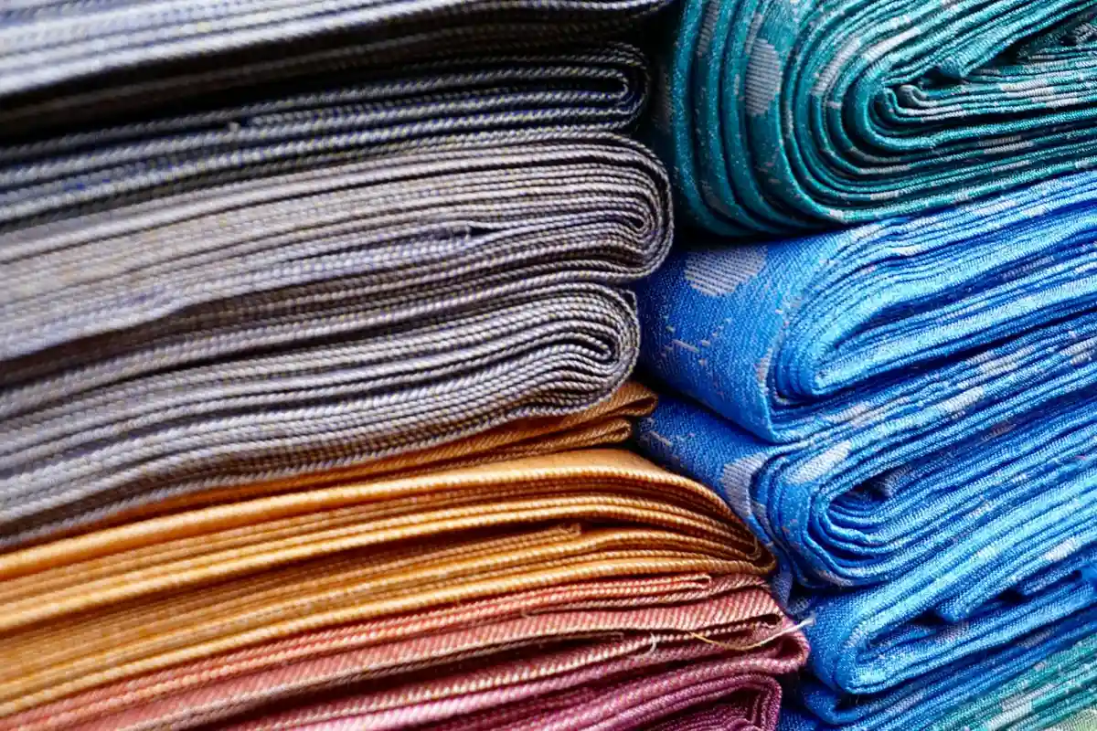 Stacks of folded fabric in gray, orange, pink, and blue hues, representing textile materials and sustainable production.