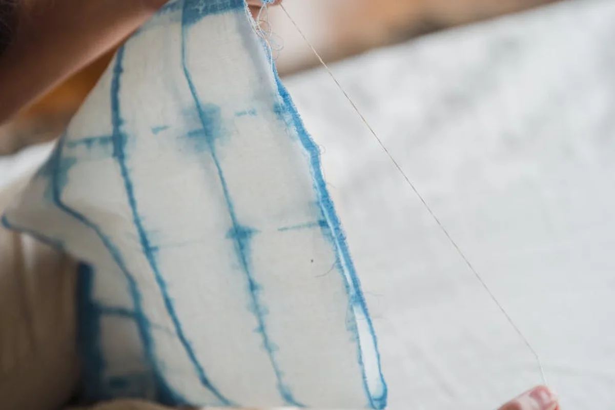 Close-up of a hand holding a white fabric with blue dye lines, illustrating the washing and prep step for Tencel or Lyocell fabrics.