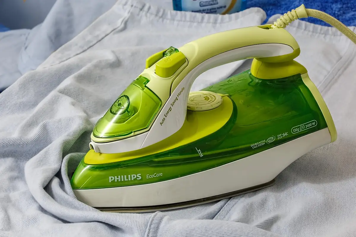 Green and white Philips steam iron resting on light gray fabric, illustrating prep before dyeing Tencel or Lyocell fabrics.