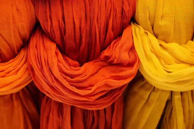 Close-up of vibrant orange and yellow Tencel/Lyocell fabrics folded and draped, showing soft texture and sheen.