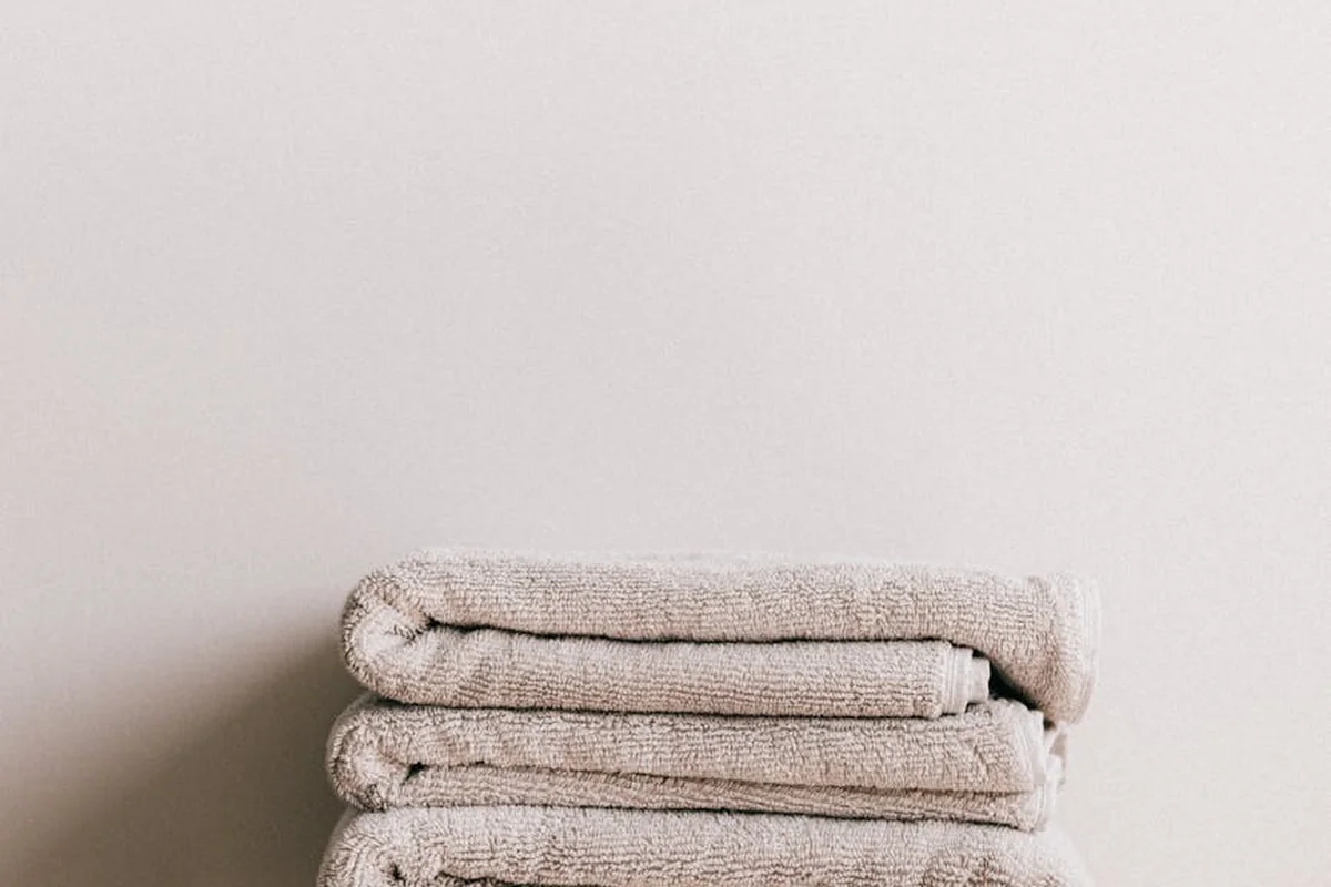 A neat stack of folded beige towels on a light, neutral background.
