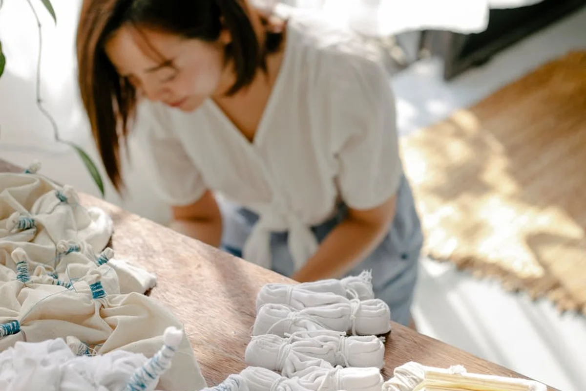 A textile professional in a white top leans over a wooden table, examining folded fabric swatches and bundles.